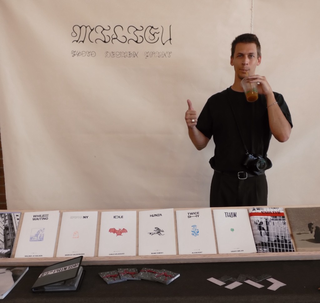 Milieu's table at a market — zines and prints laid out beneath the banner